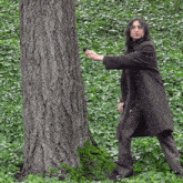 a man in a trench coat is standing next to a tree in the woods