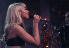 a blonde woman singing into a microphone in front of a christmas tree