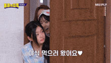 two girls are peeking out from behind a wooden door with mu-ply written on the bottom right