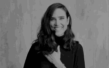 a black and white photo of a woman laughing while holding her hand to her chest .