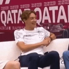a man is sitting on a couch in front of a sign that says qatar on it .