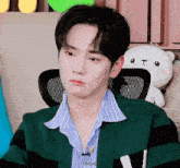 a young man wearing a green and black striped sweater is sitting in a chair