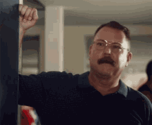 a man with glasses and a mustache is leaning against a wall and making a face .