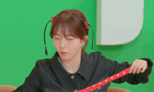 a woman wearing a black jacket and a red headband is holding a red polka dot belt .
