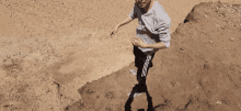a boy in a grey shirt and black pants is standing on a sandy hill