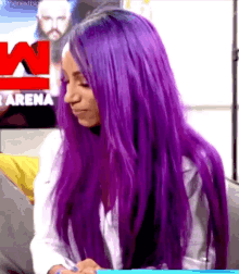 a woman with long purple hair is sitting on a couch and writing on a piece of paper .