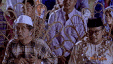 a man in a plaid shirt sits next to a man in a black hat with the word man laka on the bottom right
