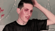 a young man with pink makeup on his face is wearing a black shirt .