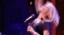 a woman is singing into a microphone on a stage in front of a crowd .