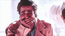 a man in a pink jacket covering his mouth with his hands