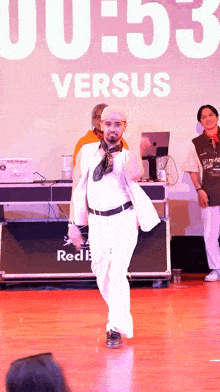 a man in a white suit is dancing in front of a sign that says versus