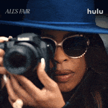a woman in a blue hat and sunglasses takes a picture with a hulu logo behind her