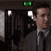 a man in a suit and tie is talking to another man in front of a green exit sign