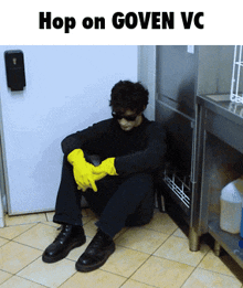 a man wearing yellow gloves sits on the floor under a sign that says hop on goven vc