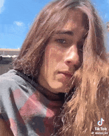 a young man with long hair is looking at the camera while wearing a t-shirt .