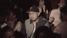 a man wearing a san francisco giants hat is sitting in a crowd of people watching a movie .
