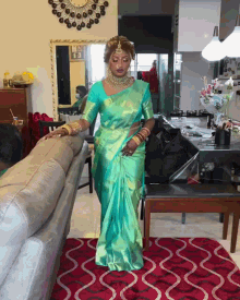a woman in a green saree is standing on a rug