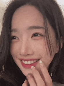 a close up of a woman 's face smiling with her hand on her chin .