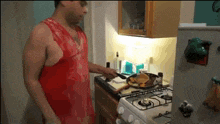 a man in a red tank top cooking on a stove