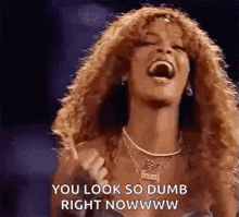 a woman with curly hair is laughing and pointing at the camera with her mouth open .