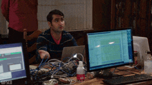 a man is sitting at a desk with a computer and a bottle of gifsco