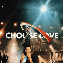 a man holding a rainbow flag on a stage with the words choose love in the background