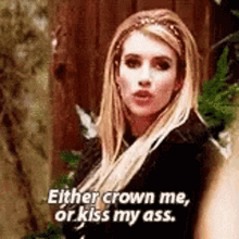 a woman is standing in front of a wooden fence and saying `` either crown me or kiss my ass . ''