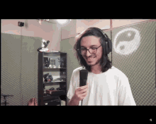 a man wearing headphones holds a microphone in front of a wall with a yin yang symbol on it