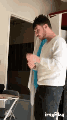 a man in a white sweater is standing in front of a door with imgplay written on the bottom right
