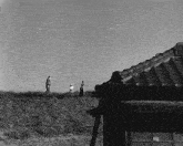a black and white photo of people standing on top of a grassy hill