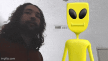 a man with long curly hair stands next to a yellow alien