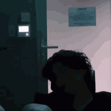 a man sitting in front of a door with a notice on the wall