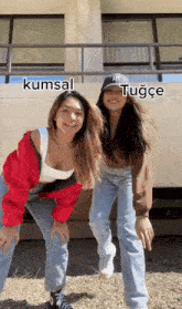 two young women are posing for a picture in front of a building . one of the girls is wearing a red jacket .