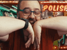 a man wearing glasses and a wrist watch stands in front of a neon sign that says ' polis '