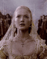 a woman wearing a veil and a cross necklace looks at the camera