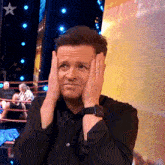 a man in a black shirt is covering his face with his hands and has a watch on his wrist