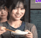 a woman is smiling while holding a plate of food with chopsticks