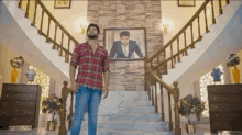 a man in a plaid shirt stands on a set of stairs in front of a picture of a man in a suit