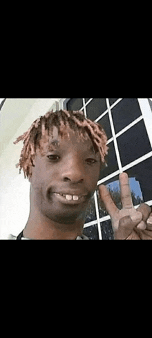 a man with dreadlocks is giving a peace sign and smiling .