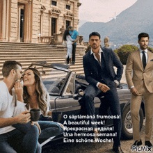 a man in a suit is sitting on a car next to a couple