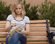 a woman sits on a park bench with an iguana on her lap