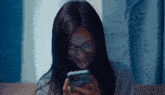 a woman wearing glasses is looking at her cell phone .