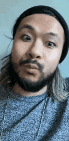 a man with a beard and long hair is wearing a beanie and a necklace .