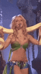 a woman in a green top and blue shorts is holding a yellow snake around her neck