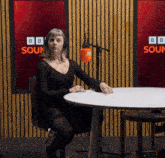 a woman wearing headphones sits at a table in front of a bbc sound screen