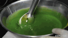 a person is mixing a green liquid in a bowl with a blender and the words made in animatica on the bottom right