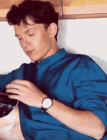 a young man wearing a blue shirt and a watch is sitting on a table .