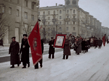 a group of people marching down a snowy street carrying flags and a picture