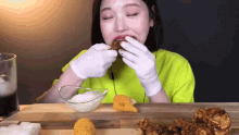a woman wearing gloves is eating a piece of chicken