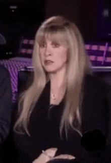 a woman with long blonde hair is wearing a black jacket and necklace .
